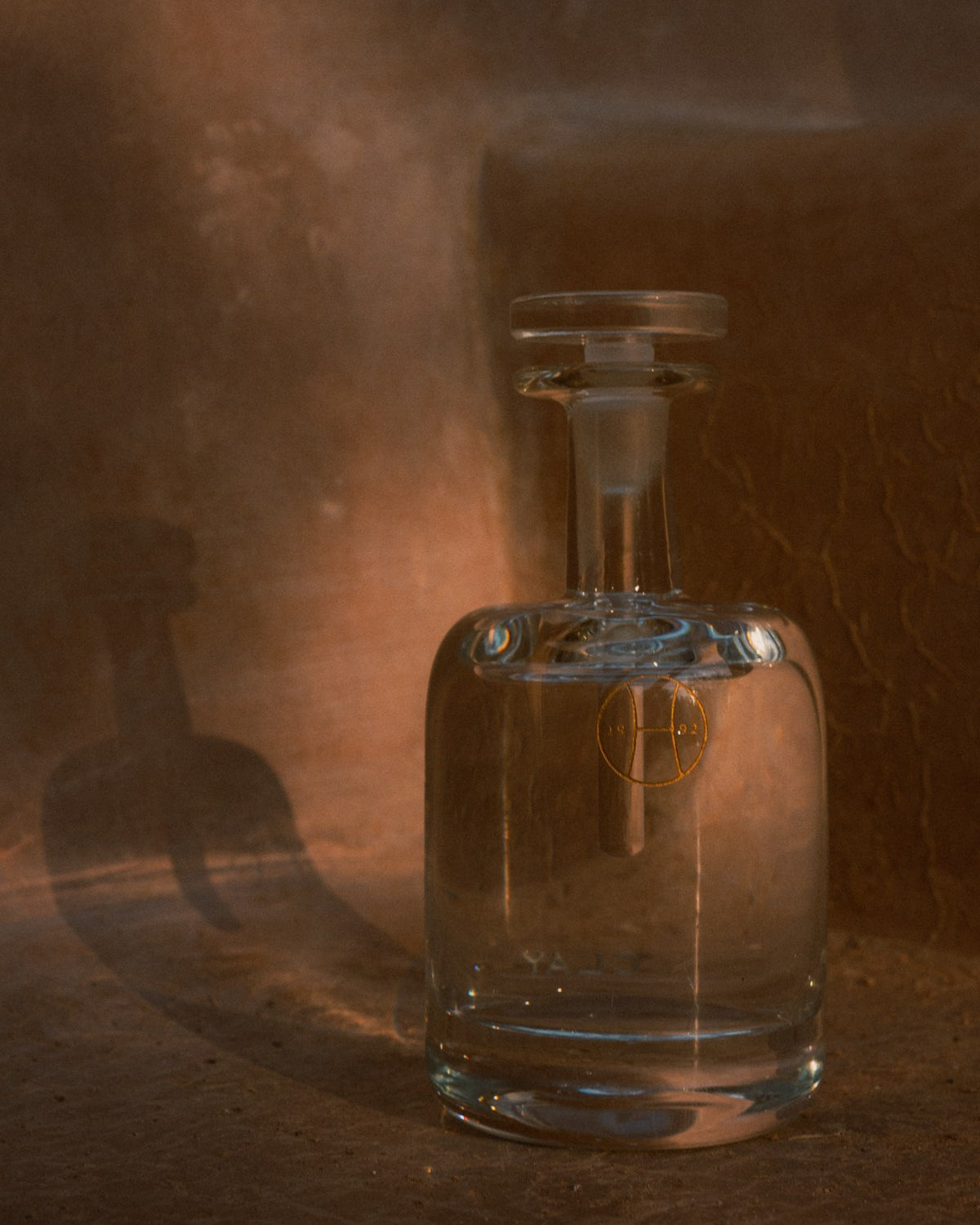 A Clay hand blown bottle against a dark ochre wall