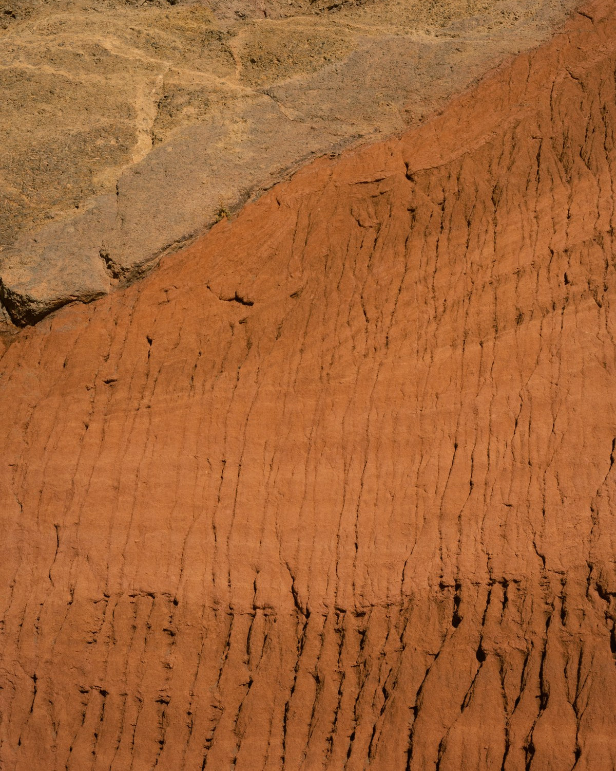 An eroded red clay bank meeting grey rock