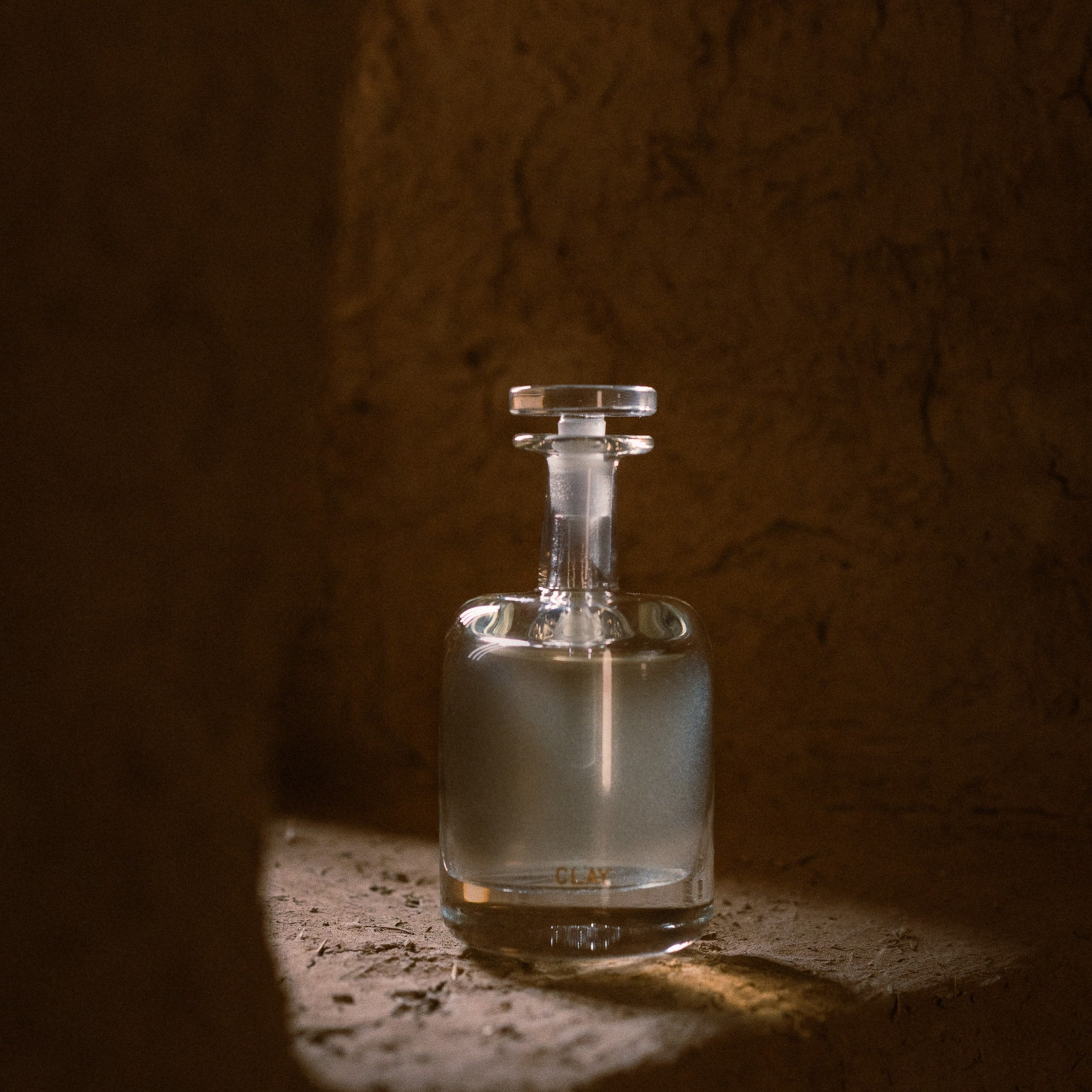 CLAY hand blown bottle lit against a clay wall