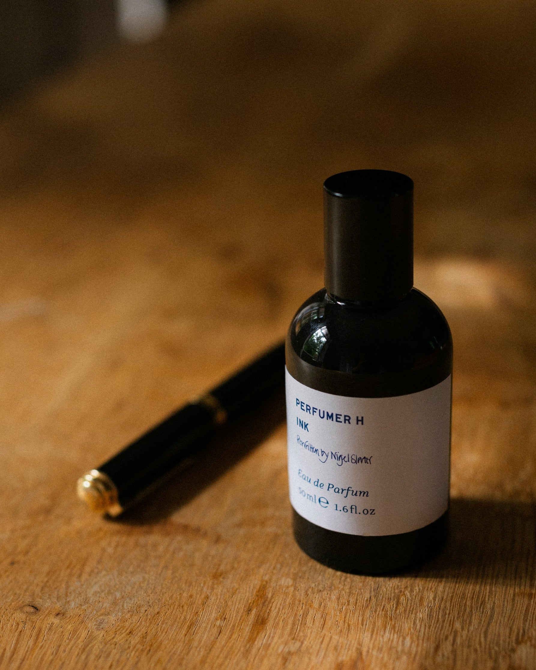 Ink Rewritten eau de parfum and a fountain pen on a wooden desk