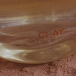 The hand blown Clay bottle in clear glass, standing on red earth