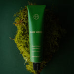 Rain Wood Hand Cream tube resting on a clump of bright green moss