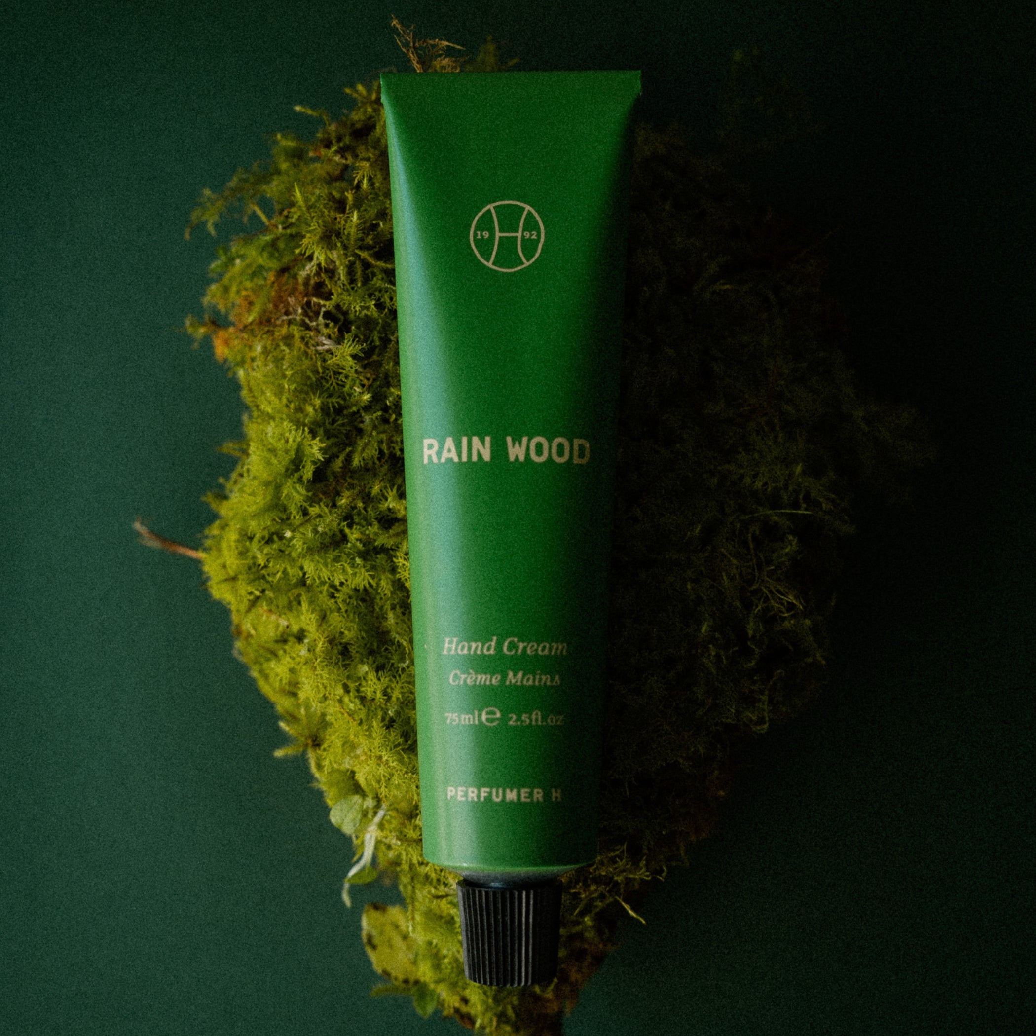 Rain Wood Hand Cream tube resting on a clump of bright green moss